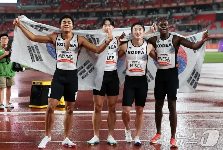 한국 대표 남자 4x100m 계주 선수 네 명이 한국 국기를展开하고 육상 트랙에 서 있는 모습이다.
