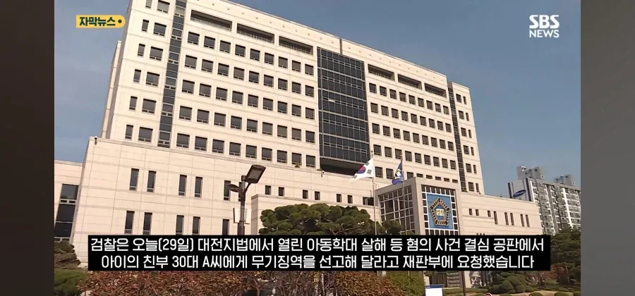 하늘 아래 서 있는 흰색 대형 건물과 그 앞에 세워진 국기 및 경찰기, 그리고 하단에 표시된 뉴스 자막이 보입니다.