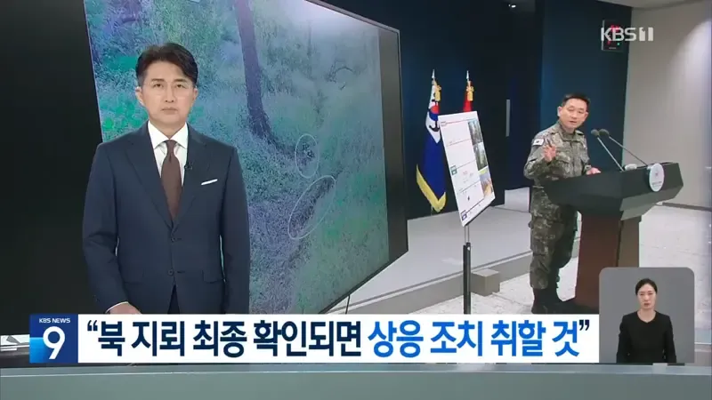 스uit를 입은 뉴스 앵커가 화면 왼쪽에 서 있고, 배경 스크린에는 초록색 숲속 지형图上 흰색 동그라미로 표시된 지뢰로 보이는 것이 있으며, 오른쪽에는 군복을 입은 인물이 연단에서 발언하고 있는 KBS 뉴스 화면이다.